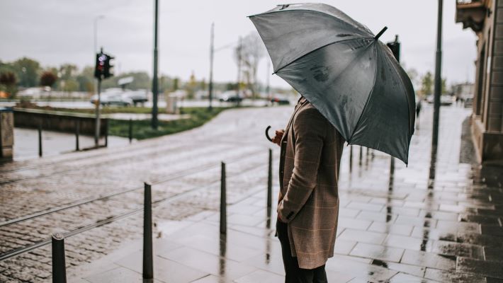 A man stands on a wet sidewalk with an open umbrella