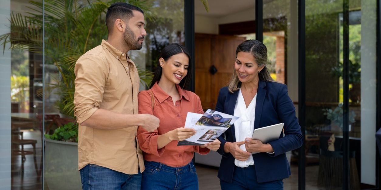 Couple talking to a real estate agent while looking at a house and checking some flyers - home ownership concepts
