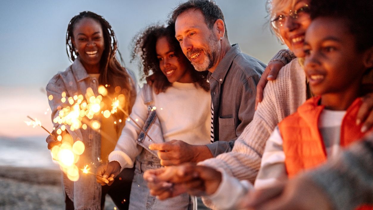 Multigenerational family holding sparklers at the beach in the evening
